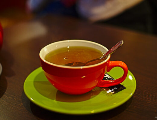 A red teacup with tea and a spoon inside rests on a lime green saucer, which itself rests on a warm-wooden tabletop.